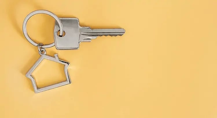 A key with a house-shaped keychain on a light surface, symbolizing home ownership or real estate.