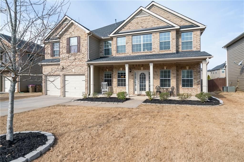 Two-story brick home with a covered porch, double garage, and dormant lawn.