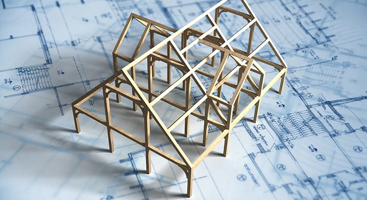 A model of a house framework made of wooden sticks, set on top of a blueprint. This image likely represents the construction or architectural planning process.