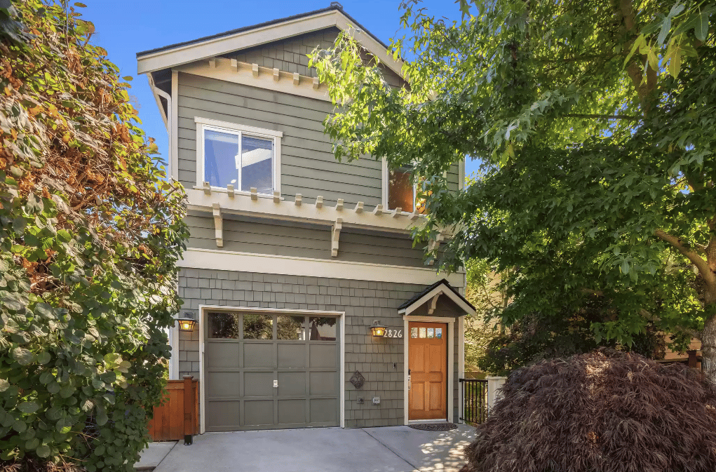Two-story gray home with a garage and wood front door, framed by mature trees.