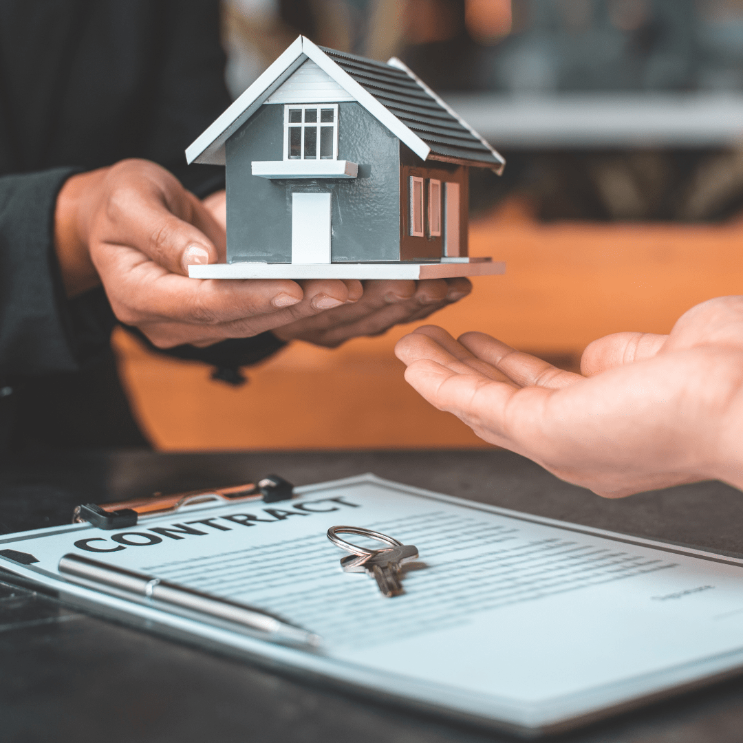 Hands exchange a model house above a contract and keys.