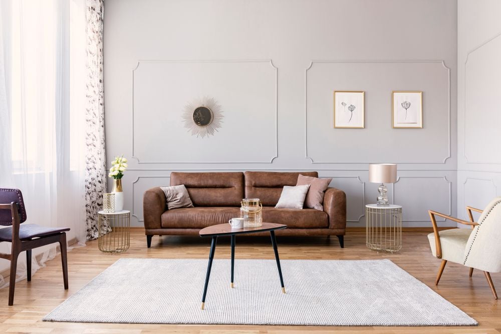 Living room with a brown leather sofa, paneled walls, and a pale rug in daylight.