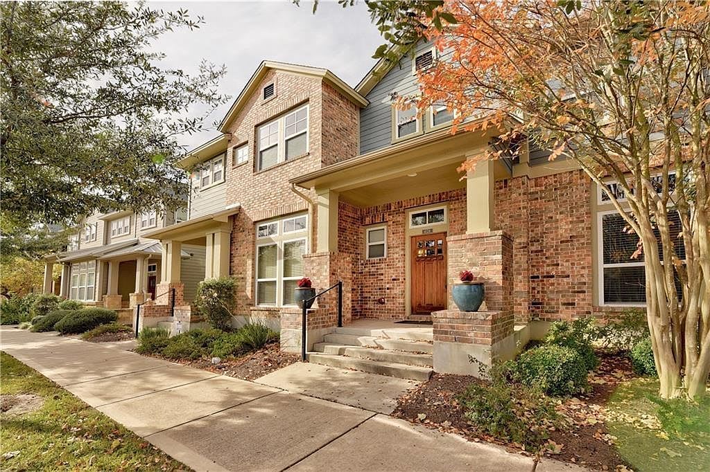 Brick townhouse with a covered entry, front steps, and autumn trees.