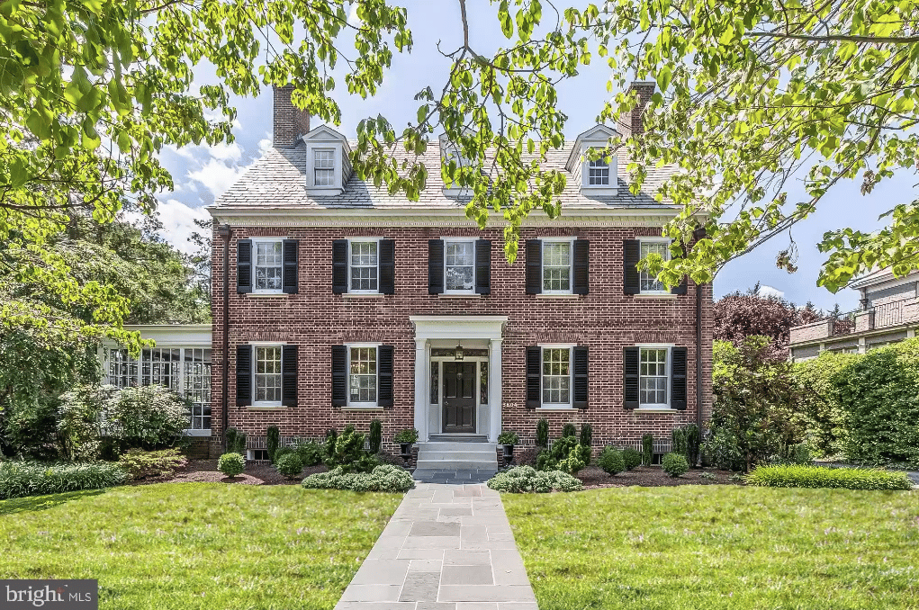 Two-story red-brick house with black shutters, a central entrance, and a stone walkway through the front lawn.