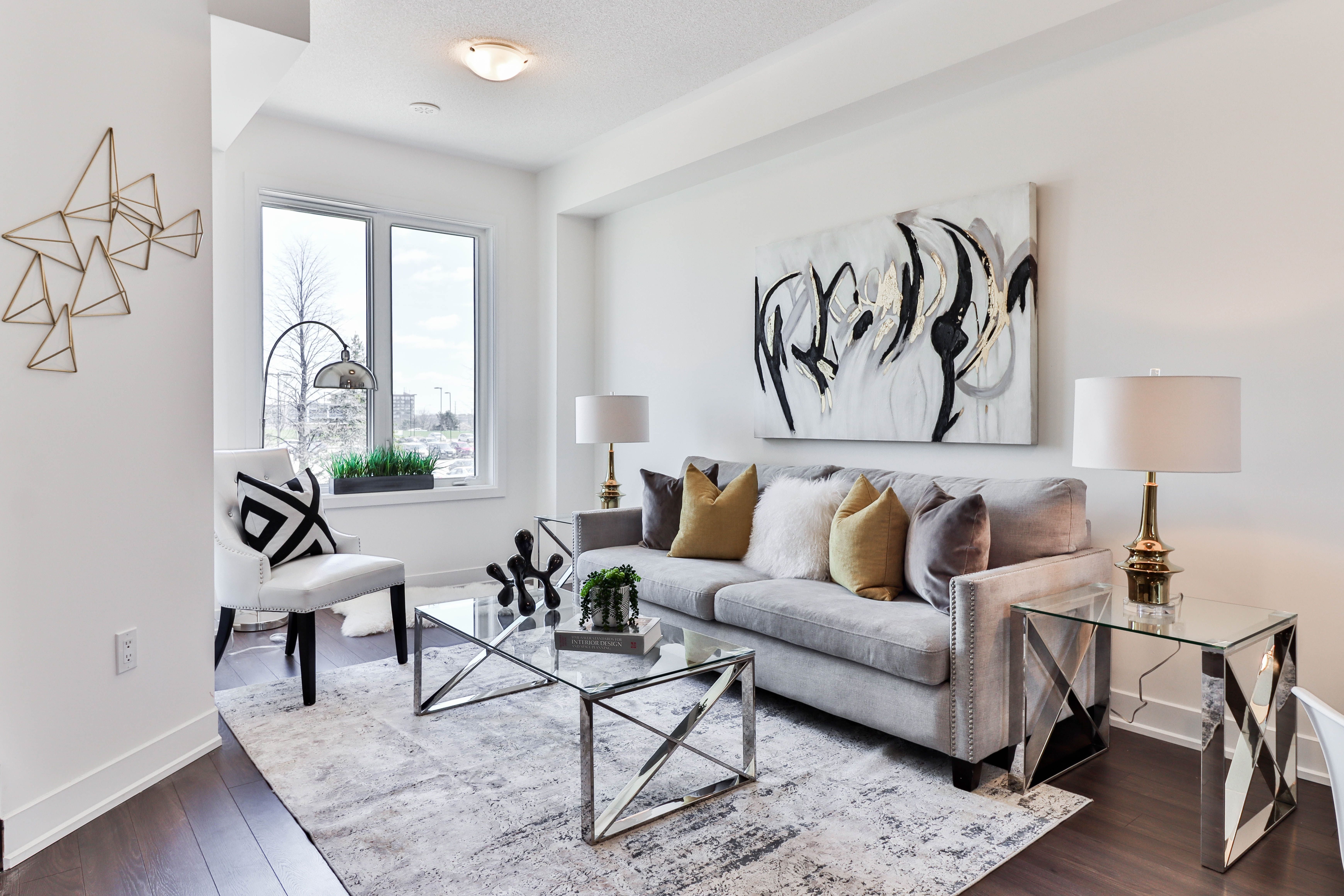 Staged living room with a gray sofa, mustard cushions, abstract artwork, and a large window.