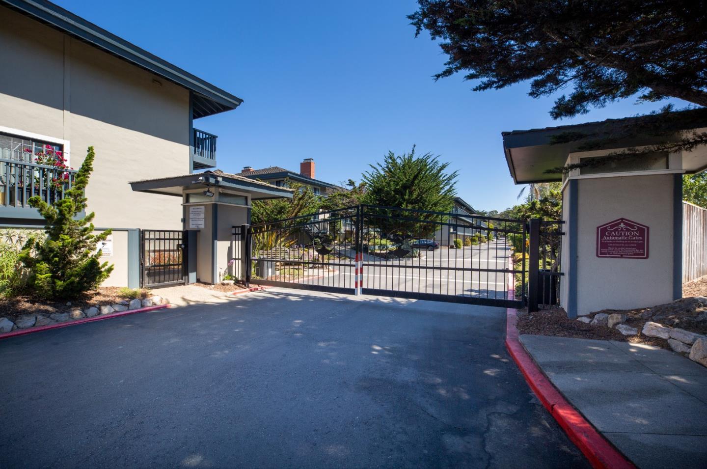 Gated residential entrance with a black metal driveway gate and two gatehouses.