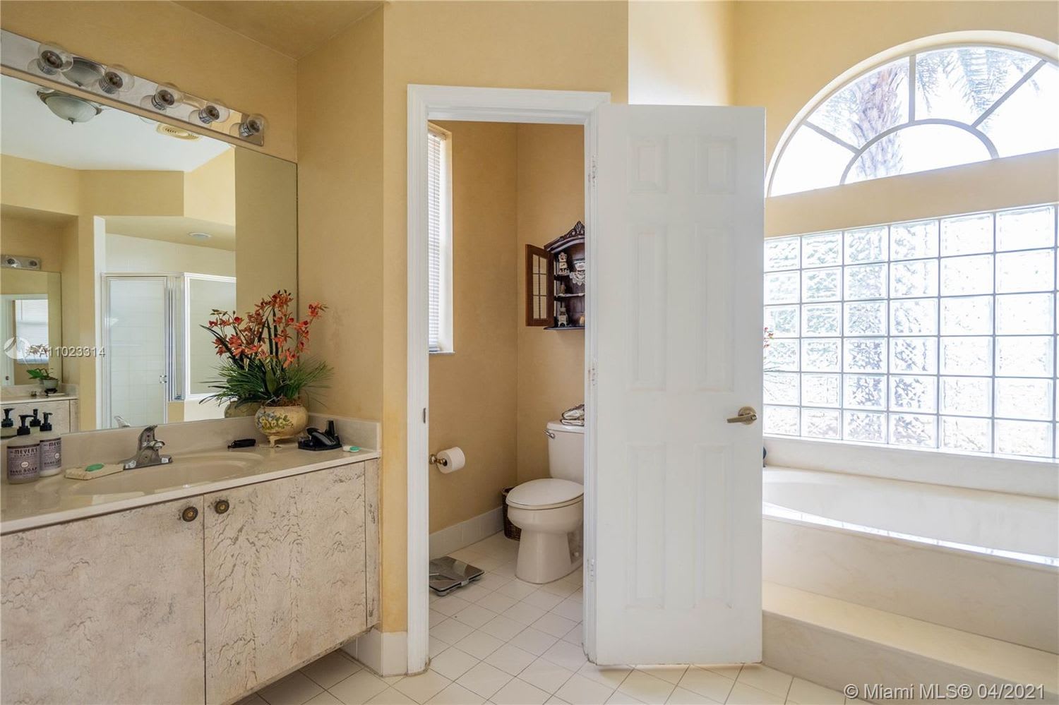 Bathroom with a marble-pattern vanity, separate toilet alcove, and large glass-block window.