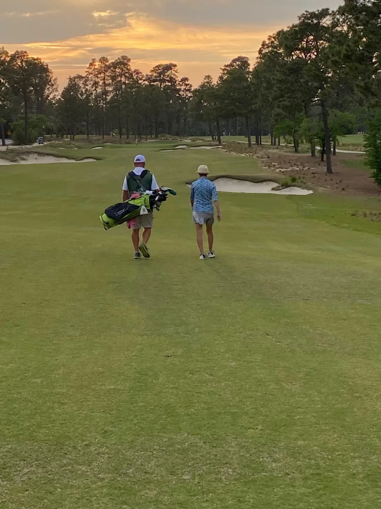 Two individuals are strolling on a golf course at sunset, creating a serene and picturesque atmosphere.