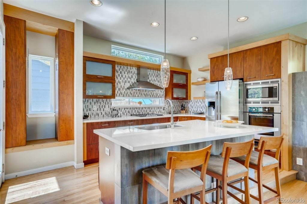 Kitchen with warm wood cabinets, patterned tile backsplash, stainless appliances, and a large island with stools.
