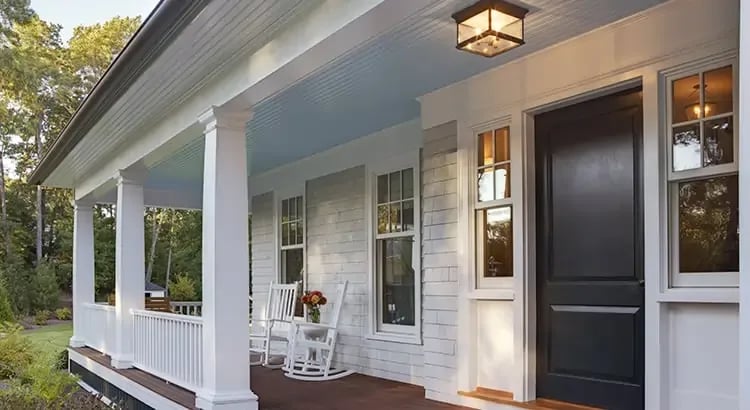  A front porch of a house with a comfortable seating area. The house has a welcoming appearance with a porch light on.