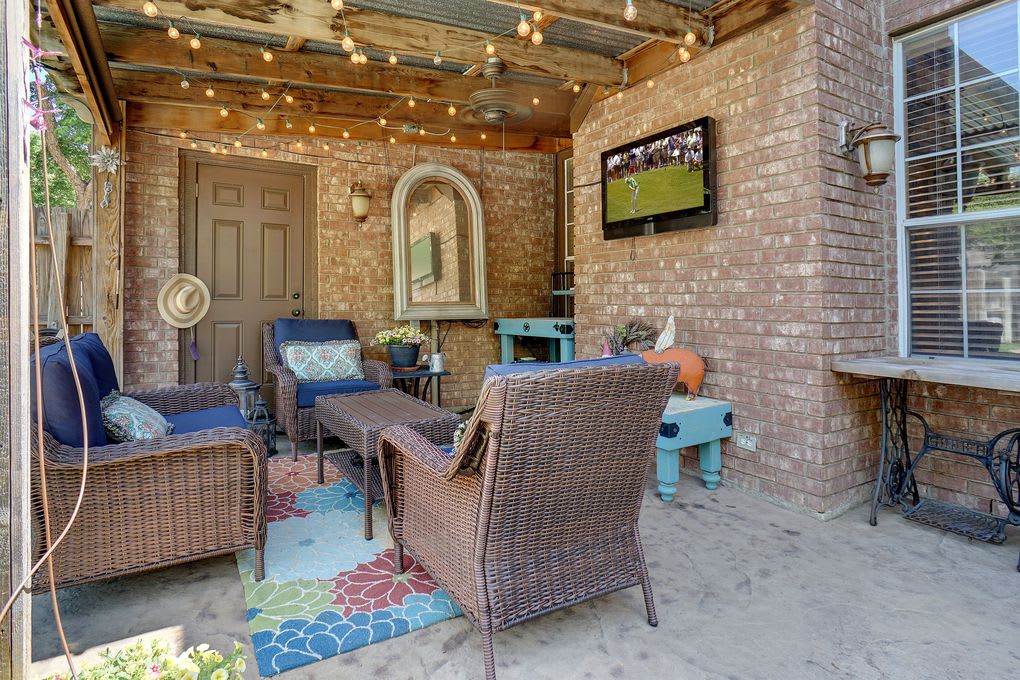 Covered brick patio with wicker seating, colorful rug, and string lights.