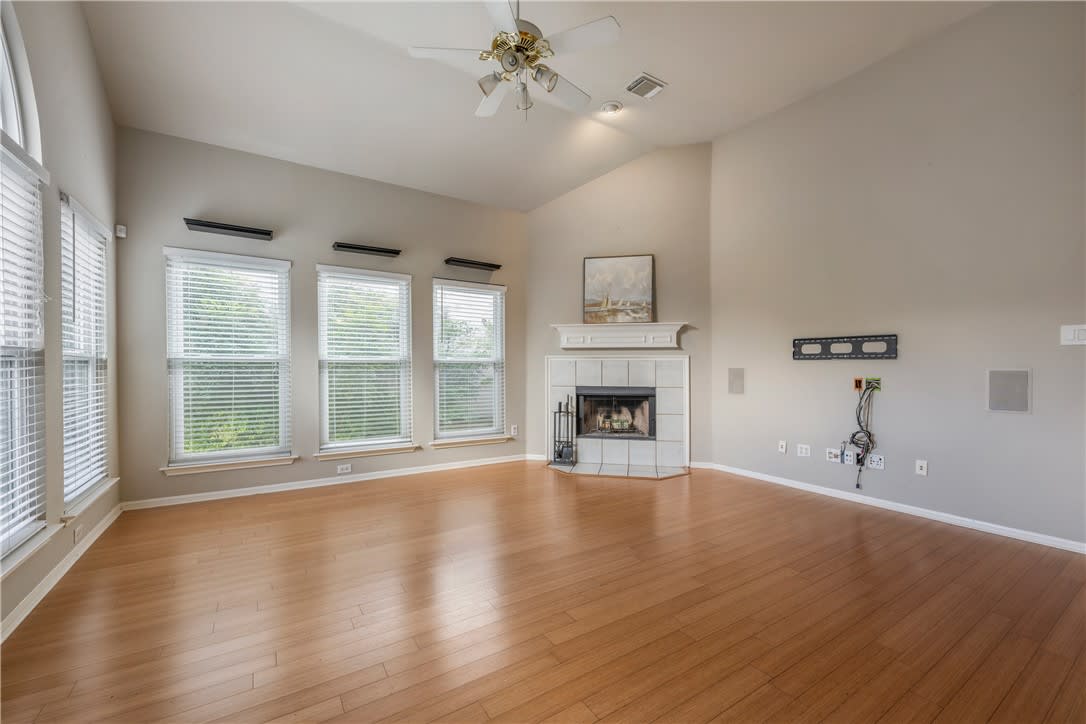 Unfurnished living room with wood floors, a tiled fireplace, and tall windows.