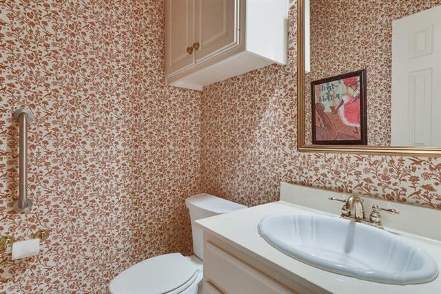 Bathroom with floral wallpaper, a white vanity, toilet, and metal grab bar.