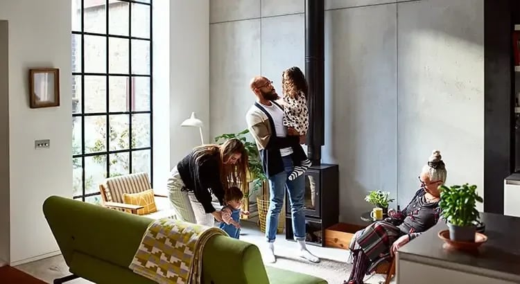 A family scene in a modern, well-lit living room. The living room has a modern and stylish design with large windows that allow natural light to flood the space.