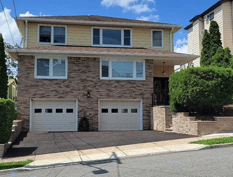 Two-story brick-and-siding house with two garage doors and a wide driveway.