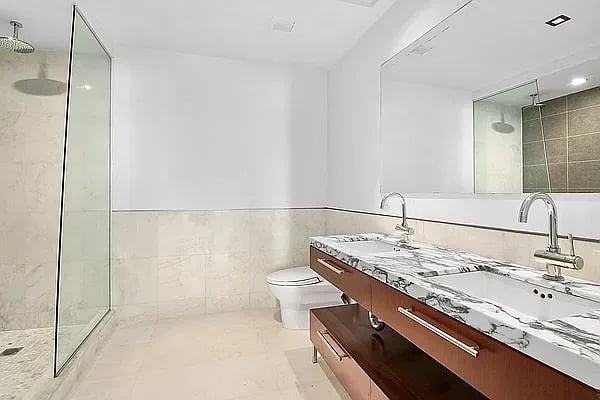 Modern bathroom with a glass shower and long double vanity topped with white-and-gray marble.