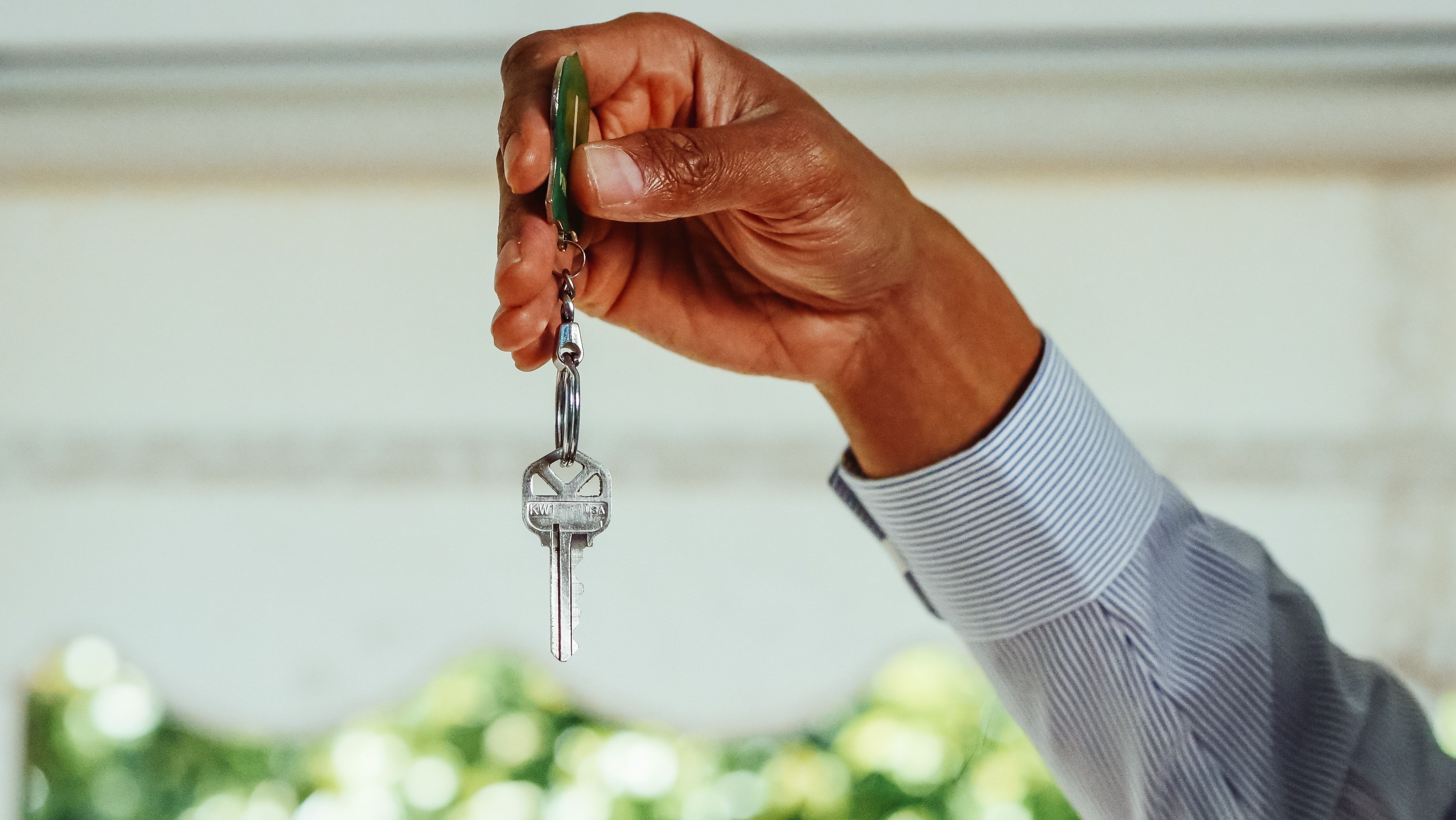 A hand holds a silver house key on a ring against a softly blurred background.