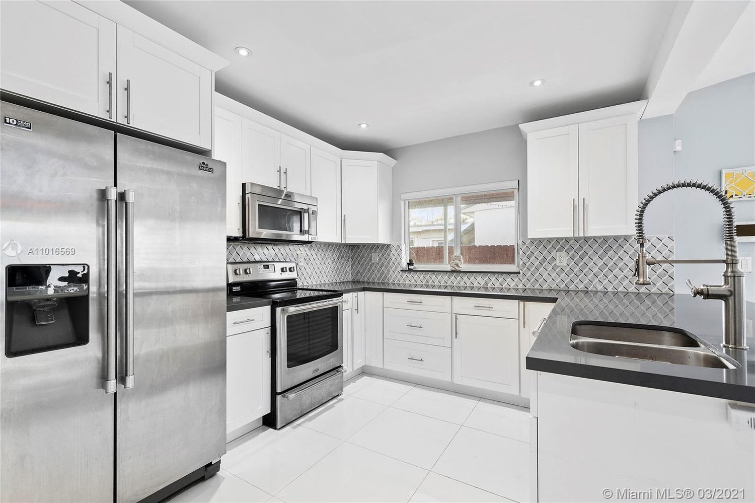 Renovated kitchen with white cabinets, stainless steel appliances, patterned backsplash, and a peninsula sink.