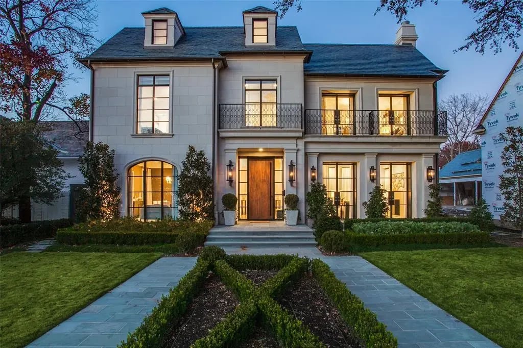 A grand, Georgian-style white mansion with large bay windows, a stone walkway, and manicured lawns with hedges and trees.