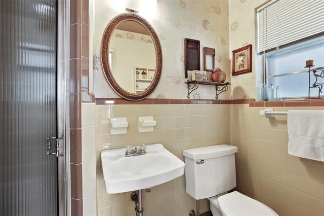 Bathroom with a pedestal sink, beige tile, oval mirror, and frosted-glass shower door.