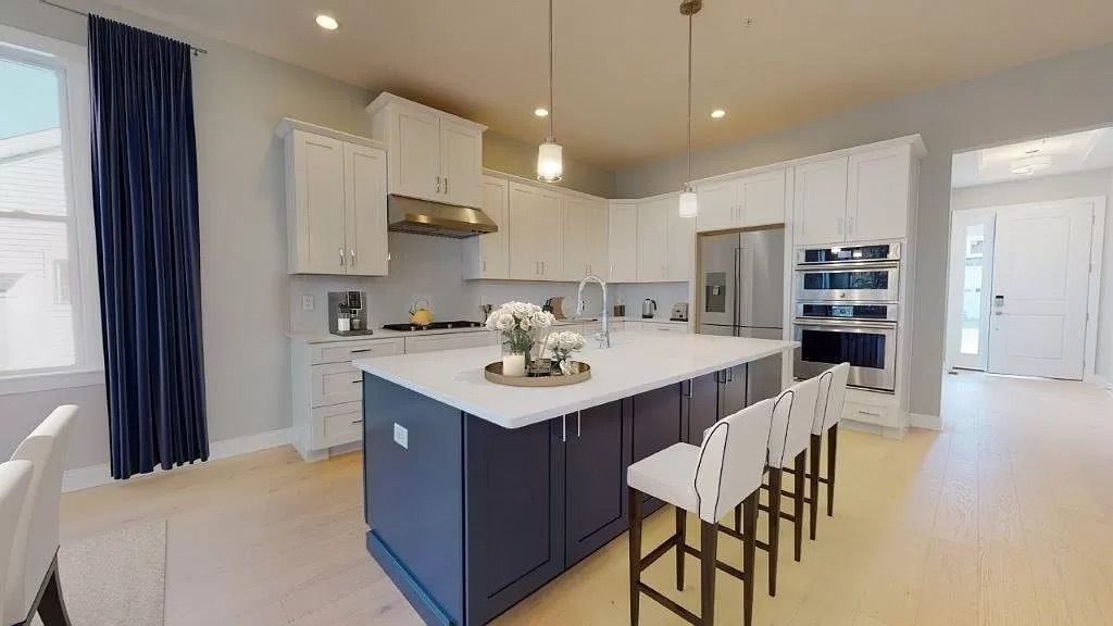 Modern kitchen with a dark blue island, white cabinets, and stainless steel appliances.