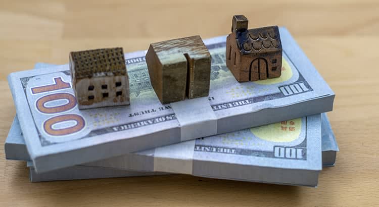 Small model houses placed on top of stacks of 100-dollar bills, symbolizing real estate and financial transactions.