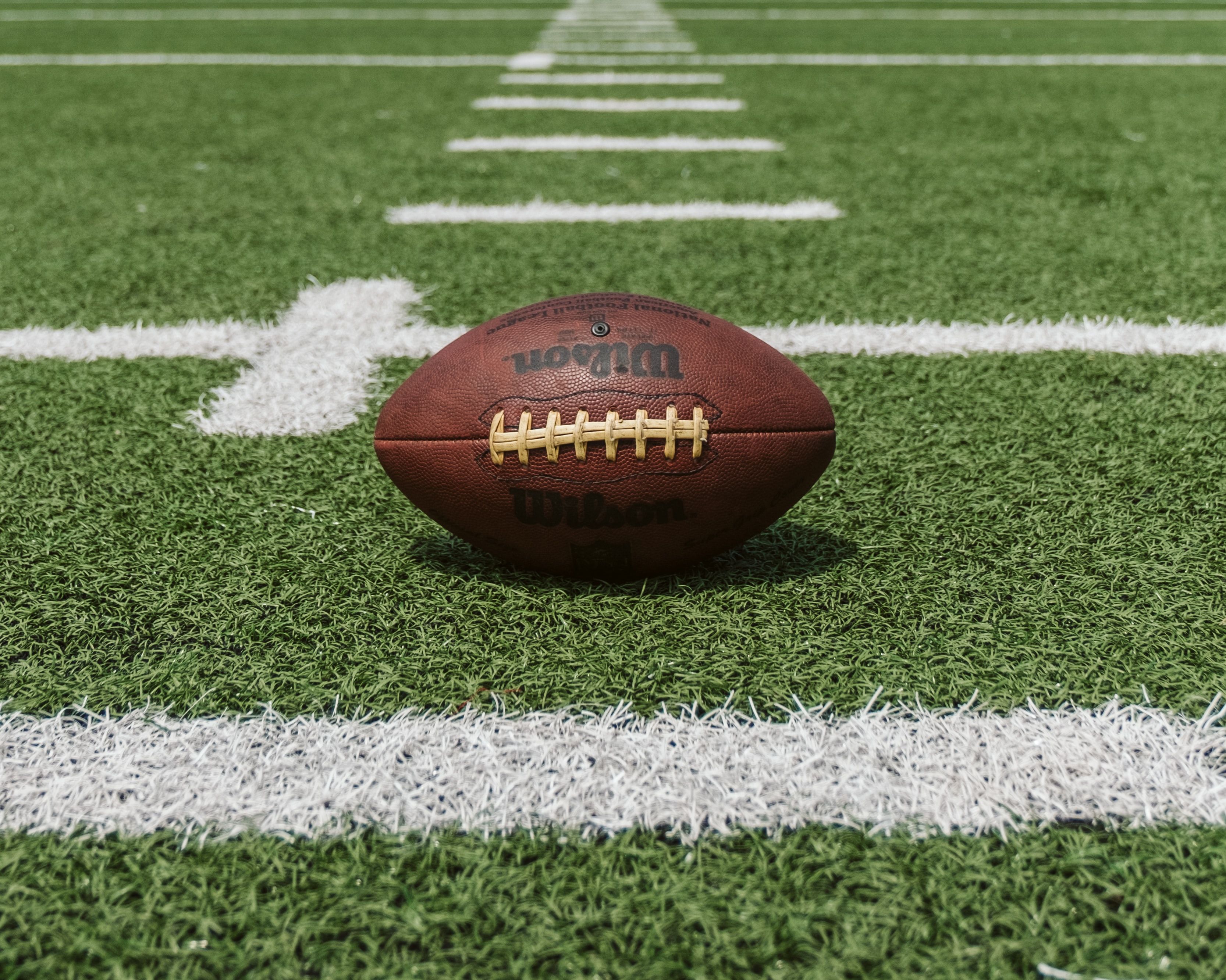 Wilson football with yellow laces resting on turf beside white field markings.