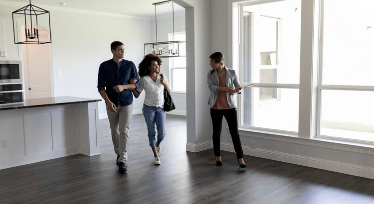 Three people, possibly real estate agent and her clients, walking through an empty house or apartment, indicating a home tour.