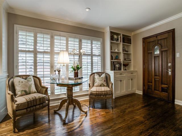 Entry sitting area with a dark wood front door, shuttered windows, upholstered chairs, and polished hardwood floors.