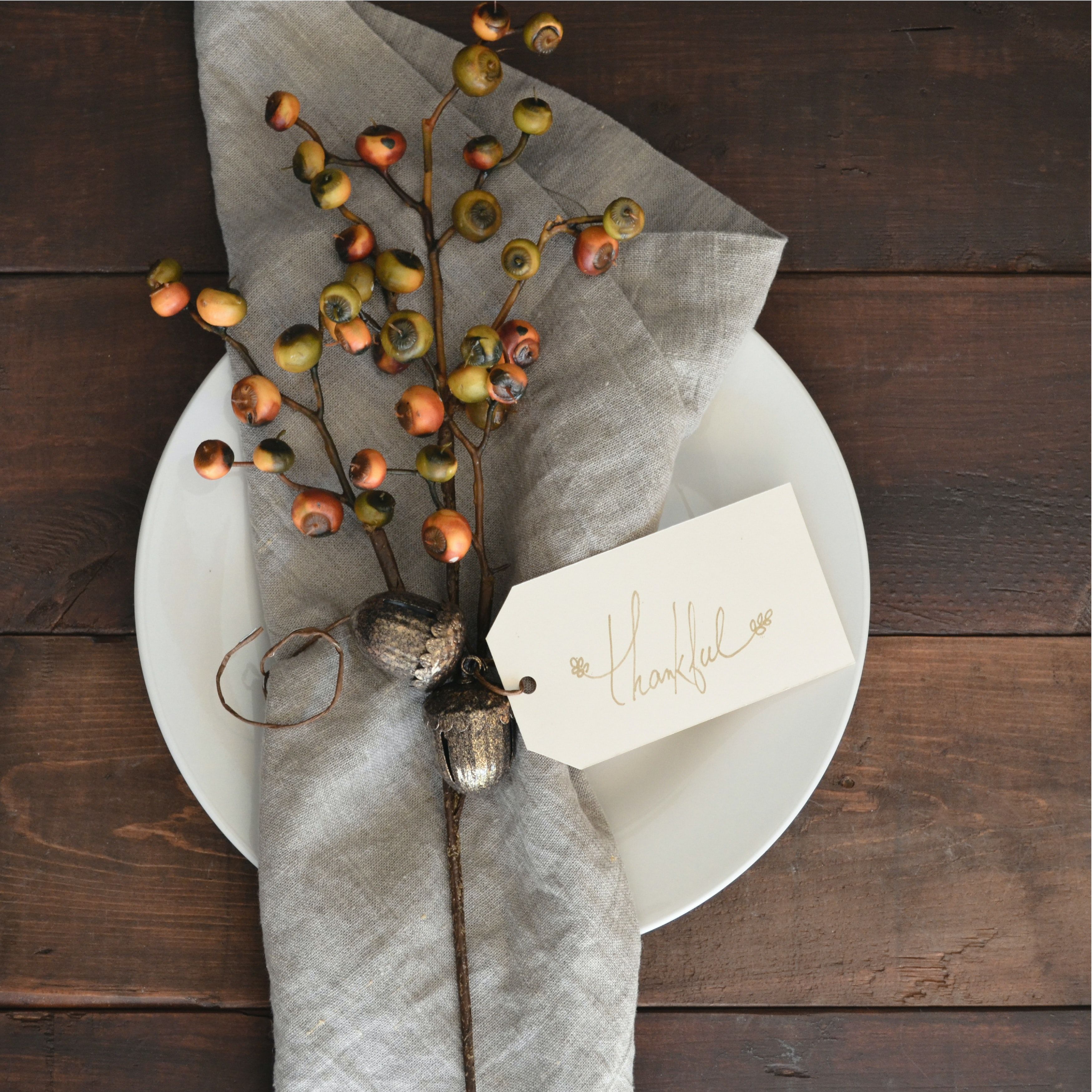 Autumn table setting with berry branches and a “thankful” place card on a white plate.