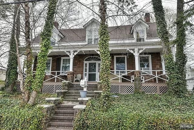 Brick house with a white-railed porch, dormer windows, and ivy-covered trees.