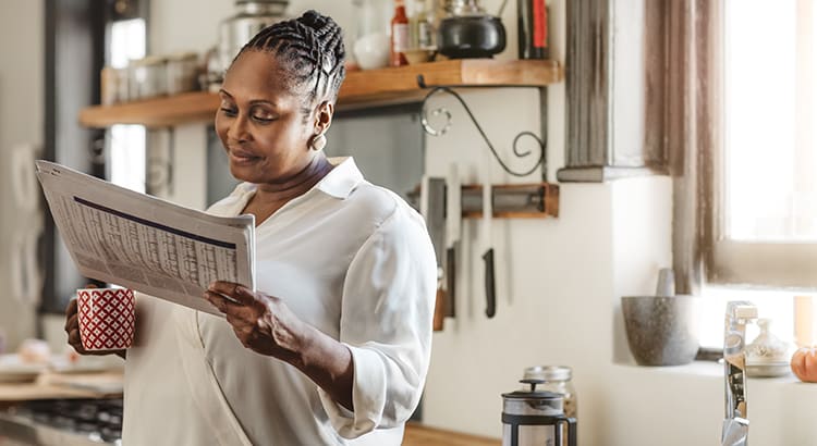 A photo of a woman reading a newspaper or document in a home setting, suggesting she is staying informed about real estate or market news.
