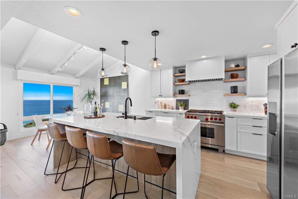 Staged kitchen with a marble island, tan bar stools, and ocean views through large windows.