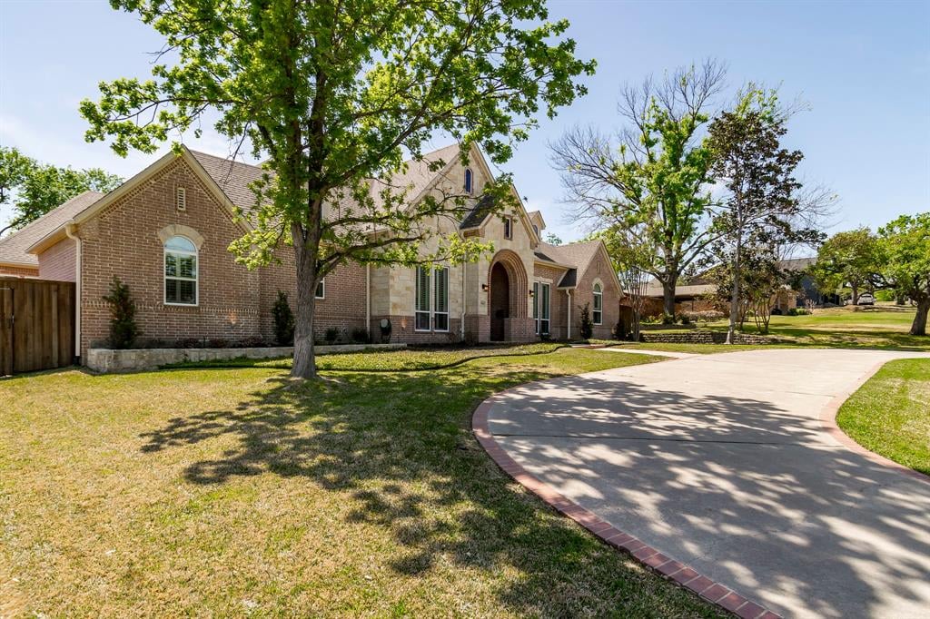 Brick and stone home with an arched entry and curved driveway beneath mature trees.