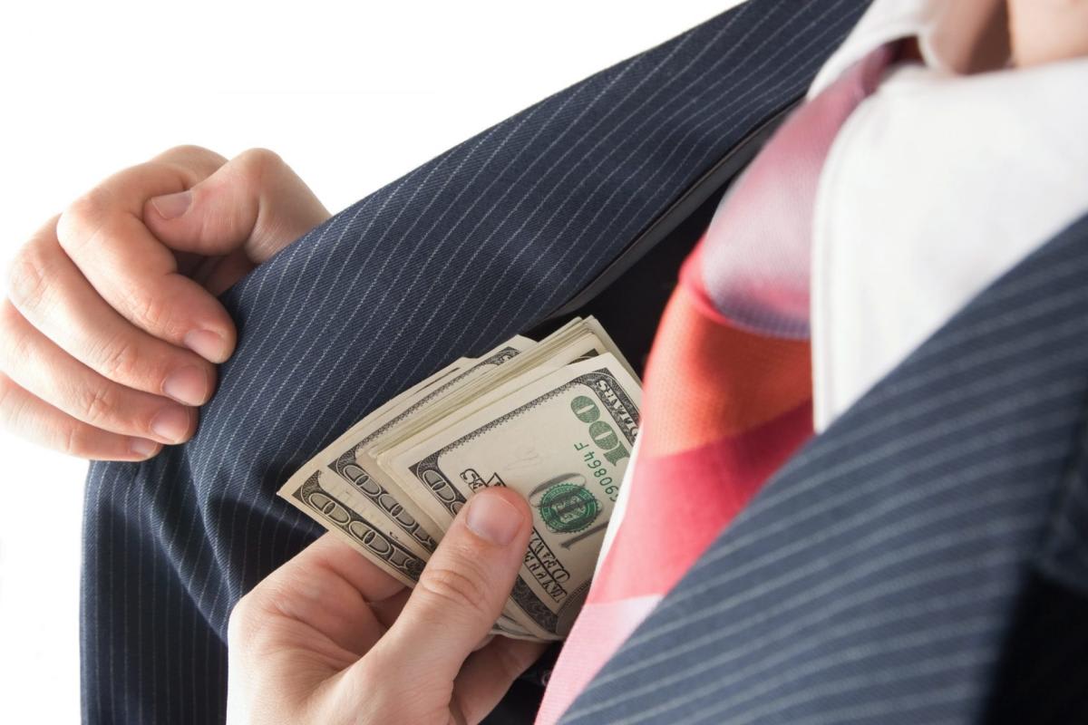 A man in a pinstripe suit pulls dollar bills from his jacket pocket.