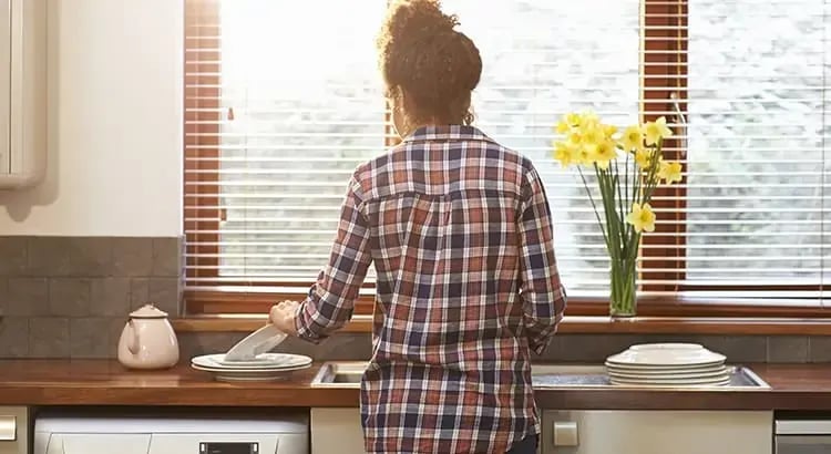 A person standing in a kitchen, back to the camera, wearing a checkered shirt. They appear to be doing something at the counter.