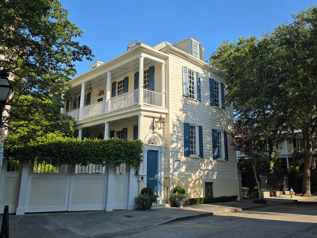 Pale yellow home with blue shutters, columned porches, balcony, and garage doors.