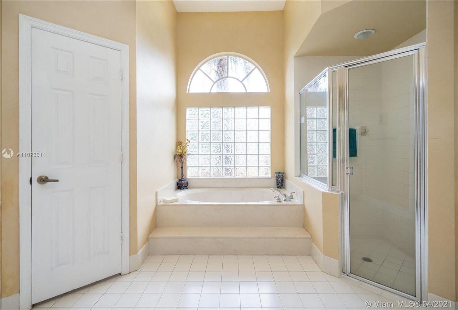 Bathroom with raised corner soaking tub beneath arched and glass-block windows, beside a glass-enclosed shower.