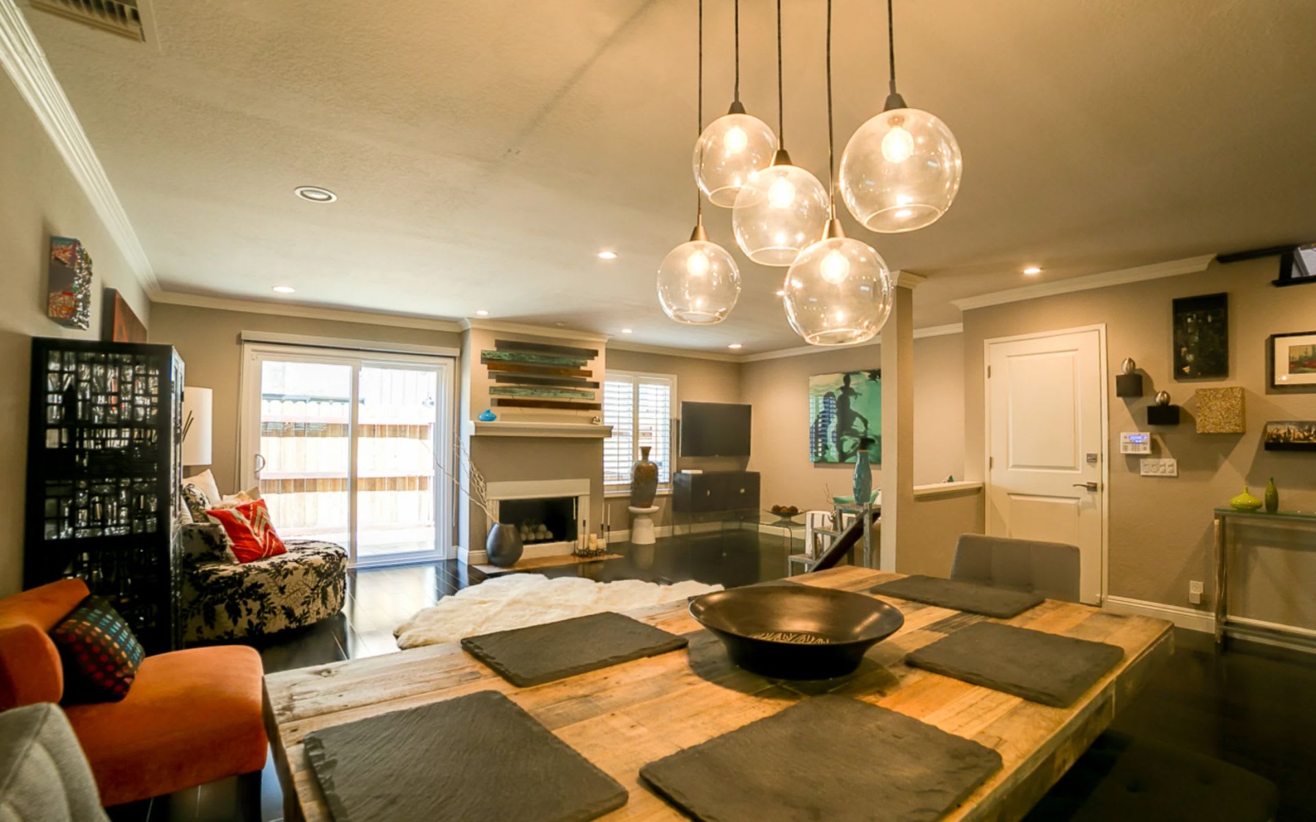Open-plan living and dining room with a rustic wood table, black fireplace, and glass pendant lights.