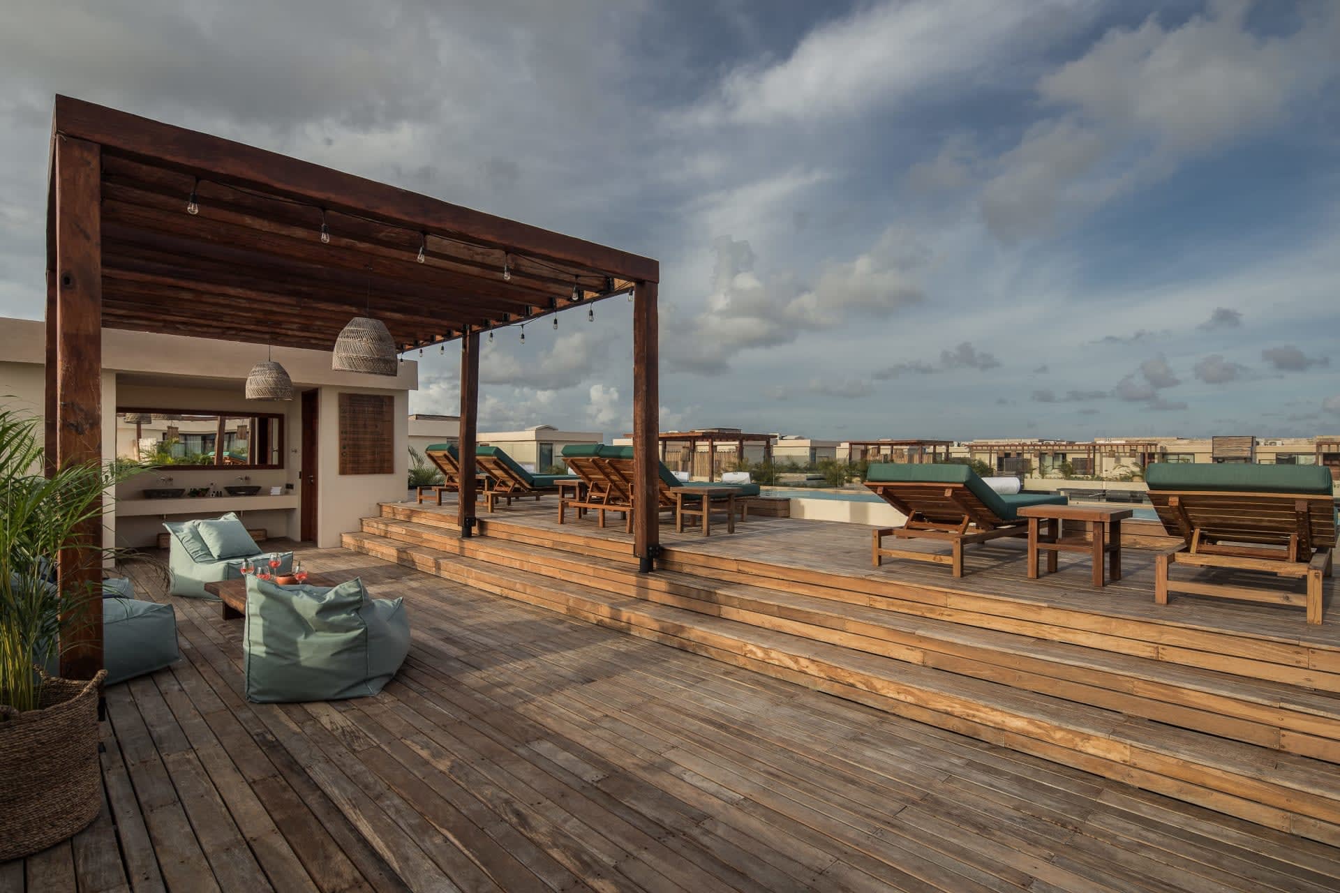 Rooftop terrace with a timber pergola, wooden decking, and rows of cushioned lounge chairs.