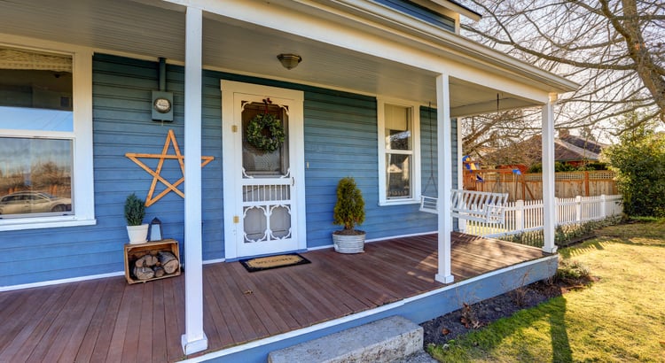 A house with a front porch and blue exterior walls. The porch has a wooden floor with a rich brown finish.