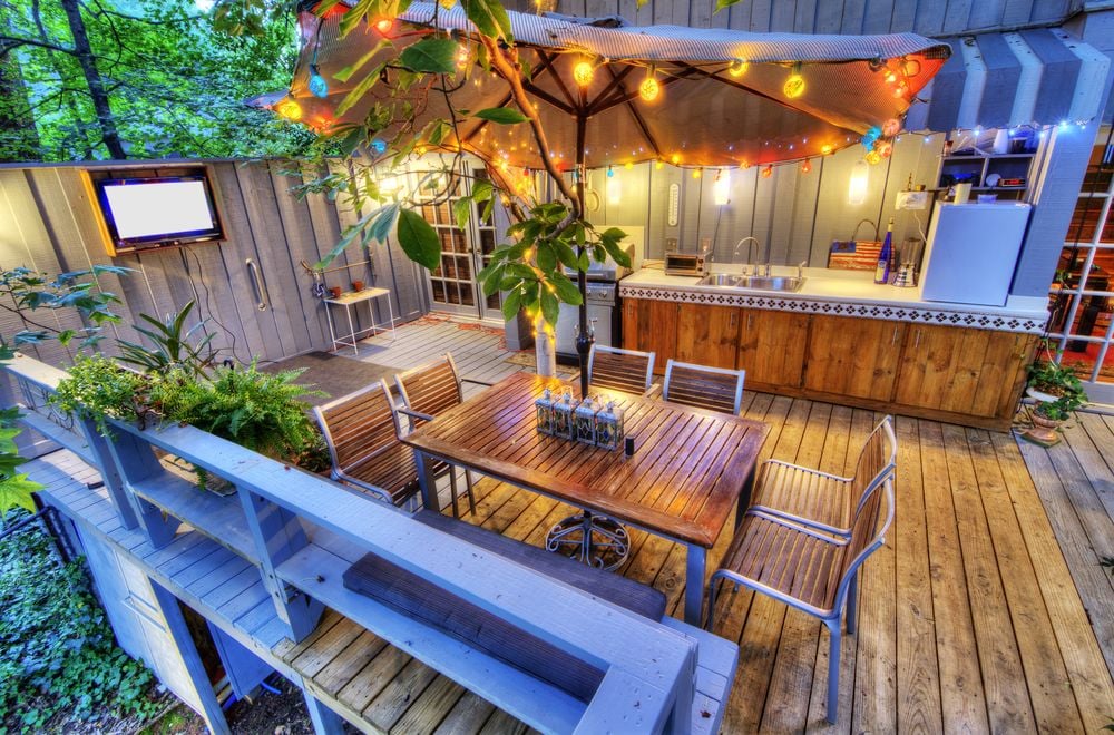 Outdoor deck with a wooden dining table, outdoor kitchen, and colorful string lights