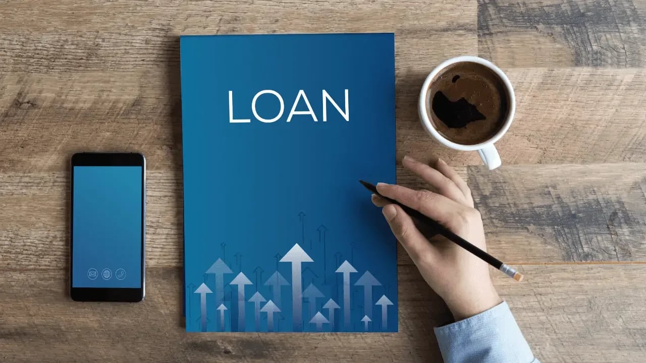 A desk with a loan application booklet, a smartphone, and a cup of coffee. The scene suggests financial planning or applying for a loan.