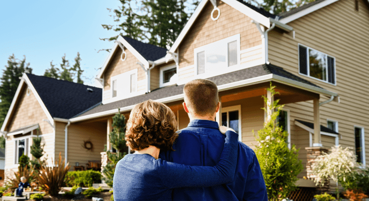 A couple stands together in front of a charming house, smiling and enjoying their time outdoors.