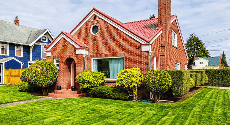 A charming house featuring a red roof, surrounded by a lush green lawn, creating a picturesque outdoor setting.