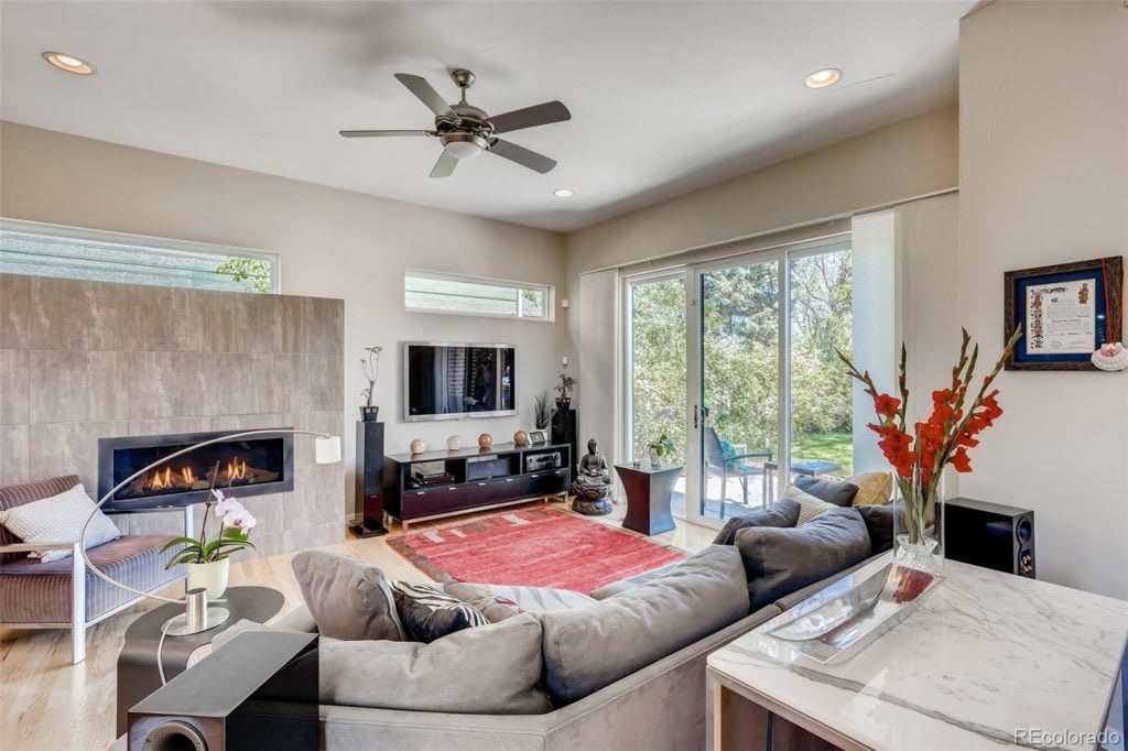 Living room with a gray sectional, stone fireplace, red rug, and sliding glass doors to the garden.