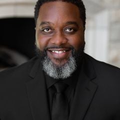 Shelton Williams in a black suit and tie, with a salt-and-pepper beard.