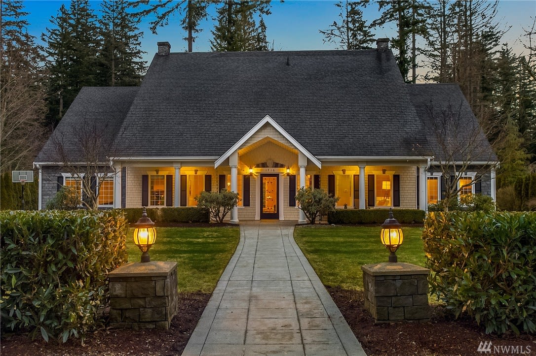 Home exterior at dusk, with a steep roof, warmly lit windows, and a lantern-lined walkway.