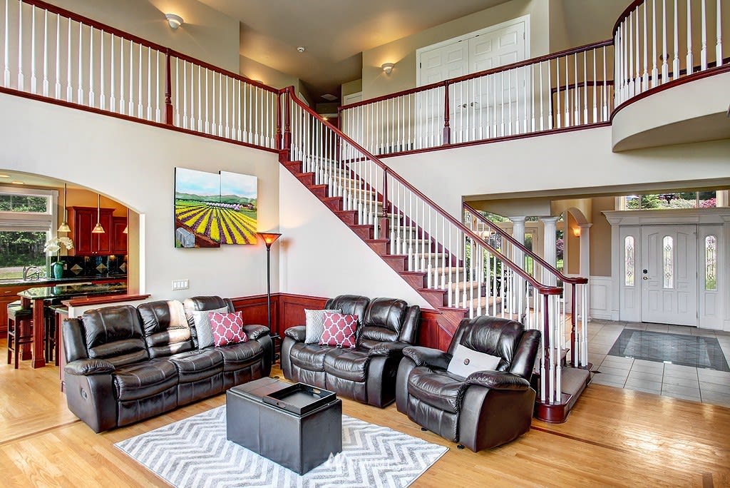 Living room with dark leather seating and a wood staircase overlooking the tiled entryway.