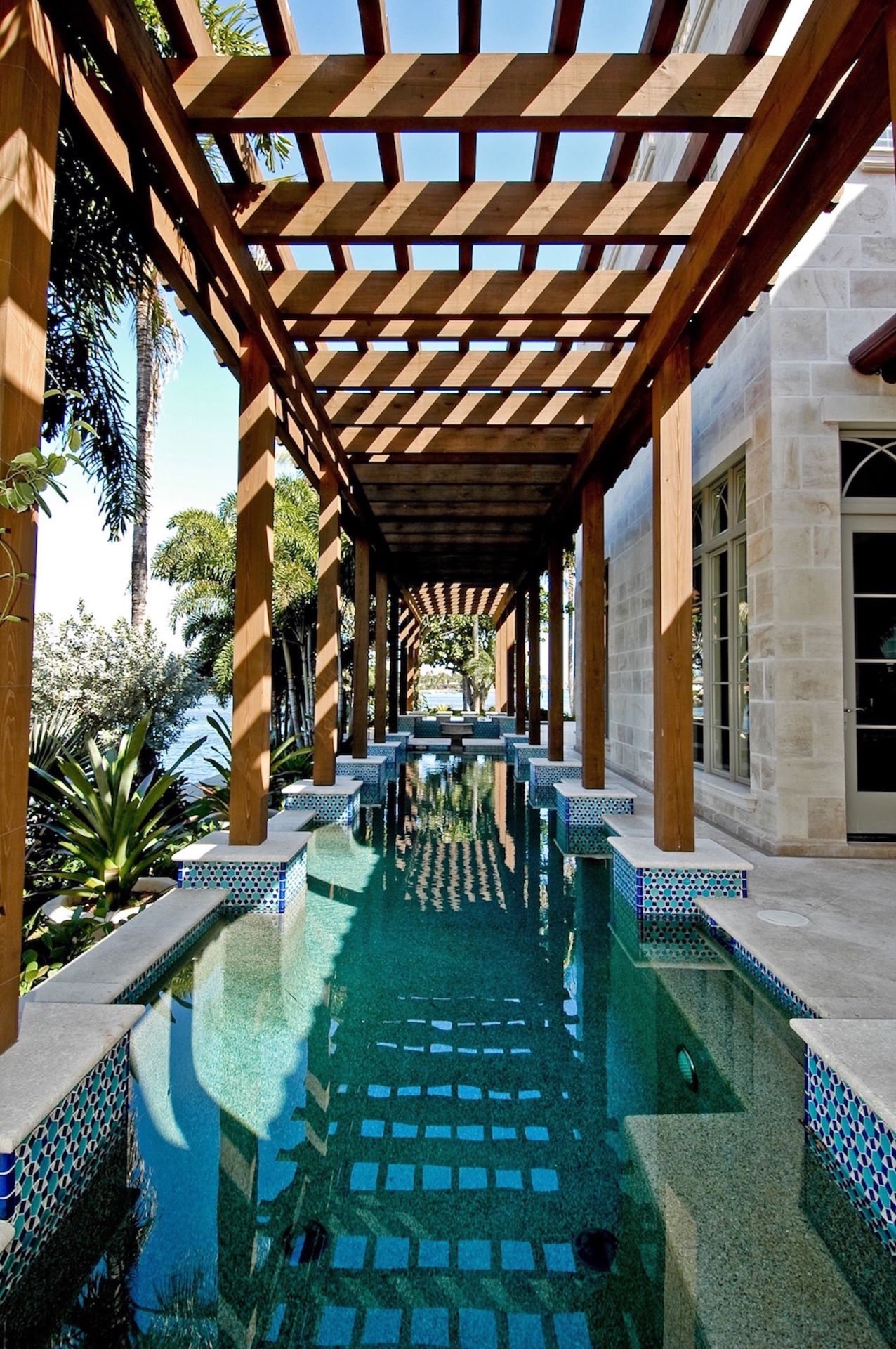 A swimming pool surrounded by a wooden walkway. The pool is blue and clear, and the walkway is made of light brown wood.